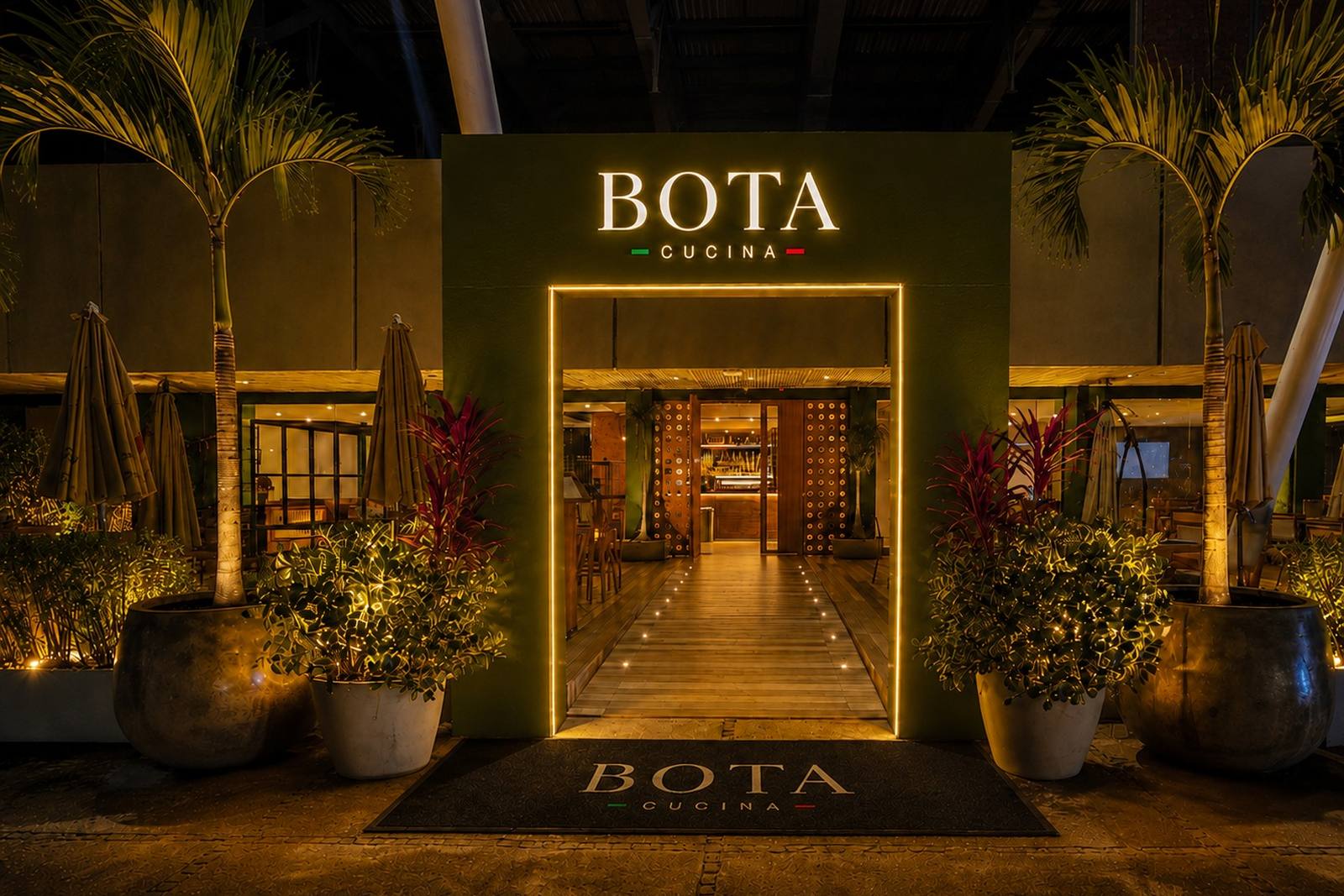 Entrada iluminada do BOTA Cucina à noite, com o letreiro BOTA CUCINA